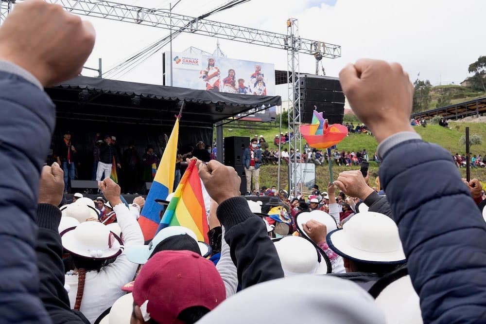 People in varied clothing in front of a stage,
facing a single speaker and cheering.